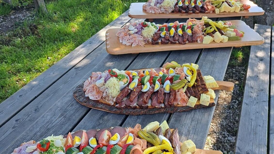 Vier Holzplatten mit regionaler Brettljause aus Käse, Wurst, Ei und Gemüse auf Holztisch bei Hirschegg-Pack.  | © Mathias Renhart