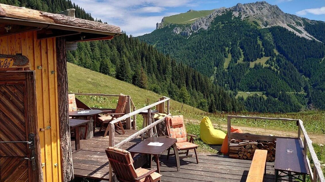Eine gemütliche Terrasse mit Holzmöbeln und Blick auf die Berge. Im Hintergrund erstrecken sich grüne Wälder und eine klare Himmel. | © Hirner