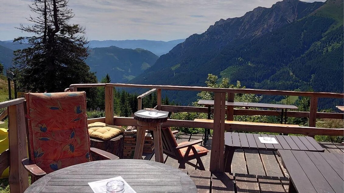 Eine gemütliche Terrasse mit Tischen und Stühlen, umgeben von Bergen und einer weiten Aussicht. Der Himmel ist klar und die Natur wirkt einladend. | © Hirner