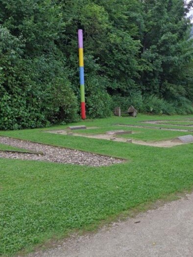 A green park with stones in the shape of letters. In the background, there are trees and a colorful mast. | © Kneippanlage Maria Rastl
