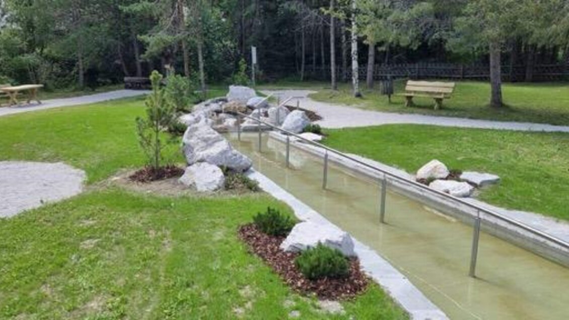 Ein ruhiger Park mit einem kleinen Wasserlauf und grünen Wiesen. Es gibt mehrere Holzbänke und schöne Pflanzenarrangements. | © Marktgemeinde Gröbming