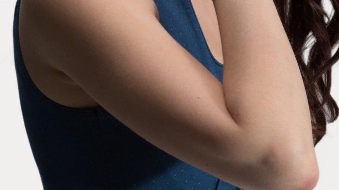 Eine Frau trägt ein traditionelles bayerisches Kleid in Blau mit einem weißen Schürzenband. Ihr arm ist mit einem eleganten Armband geschmückt. | © Knopfgeschwister