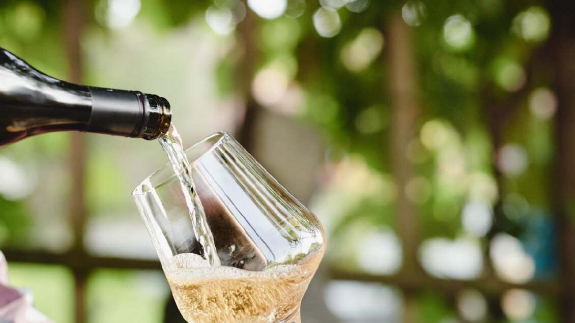 Ein Glas wird mit einem hellen Getränk gefüllt. Im Hintergrund sind verschwommene grüne Blätter zu sehen. | © Kobatl