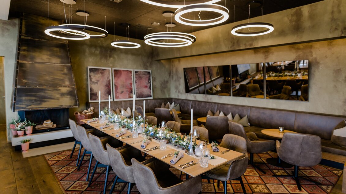 Ein eleganter Essraum mit einem langen Tisch, dekoriert mit Blumen und Kerzen. Die Wände sind in sanften Tönen gehalten und runde Lampen sorgen für eine gemütliche Atmosphäre. | © Kogel 3