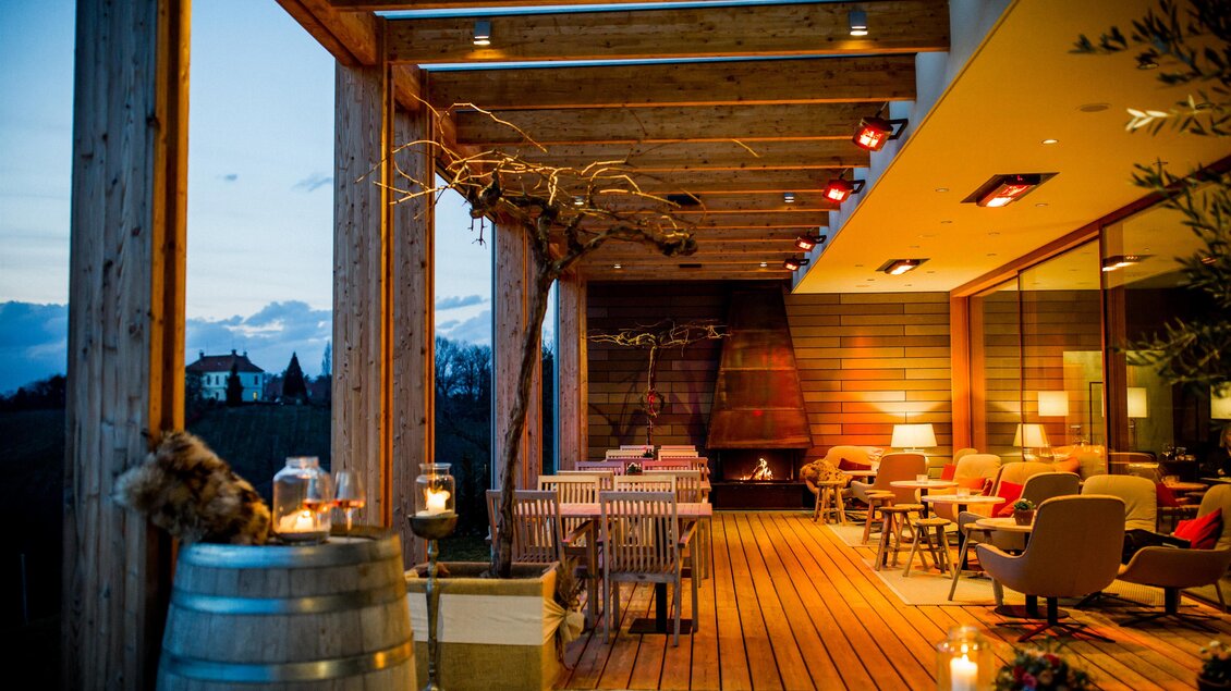 Eine gemütliche Terrasse mit stilvollen Möbeln und sanfter Beleuchtung. Im Hintergrund sind sanfte Hügel und ein Abendhimmel zu sehen. | © Kogel 3