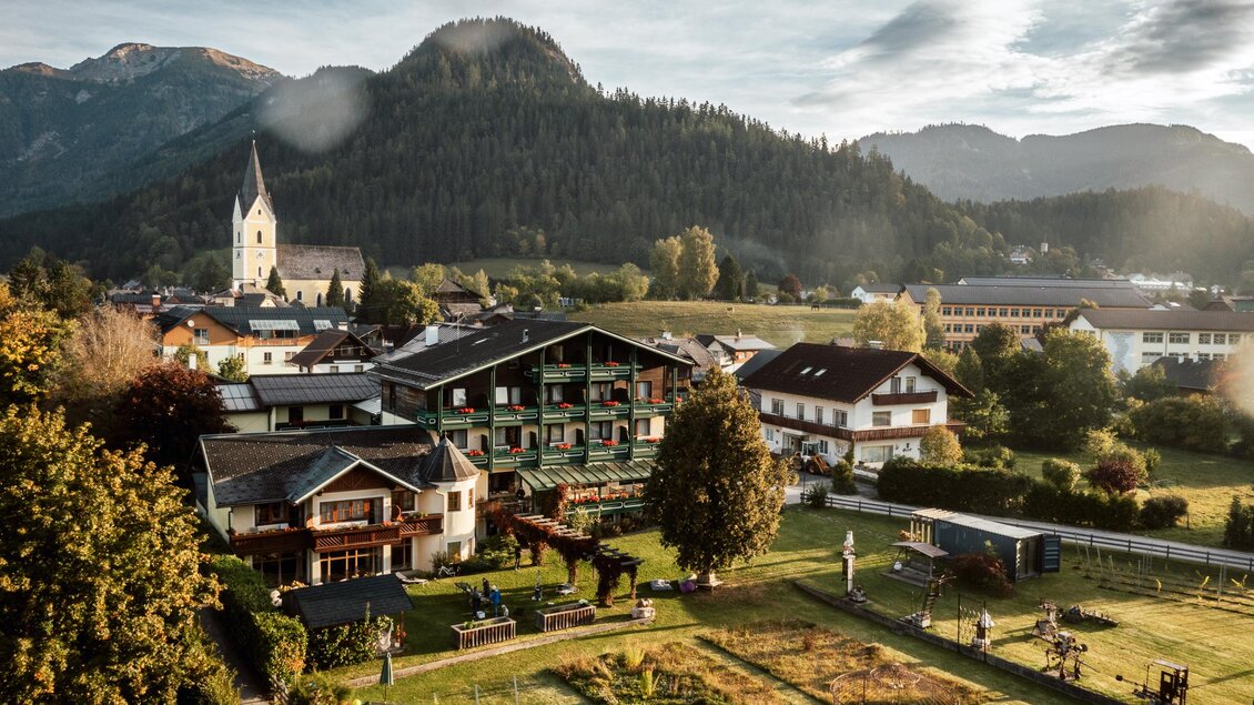 Eine malerische Landschaft mit charmanten Gebäuden und sanften Hügeln. Im Hintergrund ragen majestätische Berge in den Himmel.