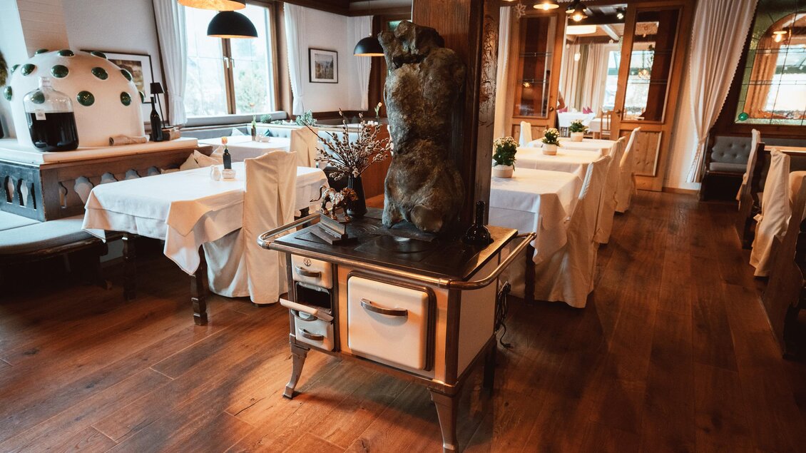 Ein stilvolles Restaurant mit weißen Tischdecken und Holzfußboden. Im Vordergrund steht ein dekorativer Herd und eine faszinierende Statue.