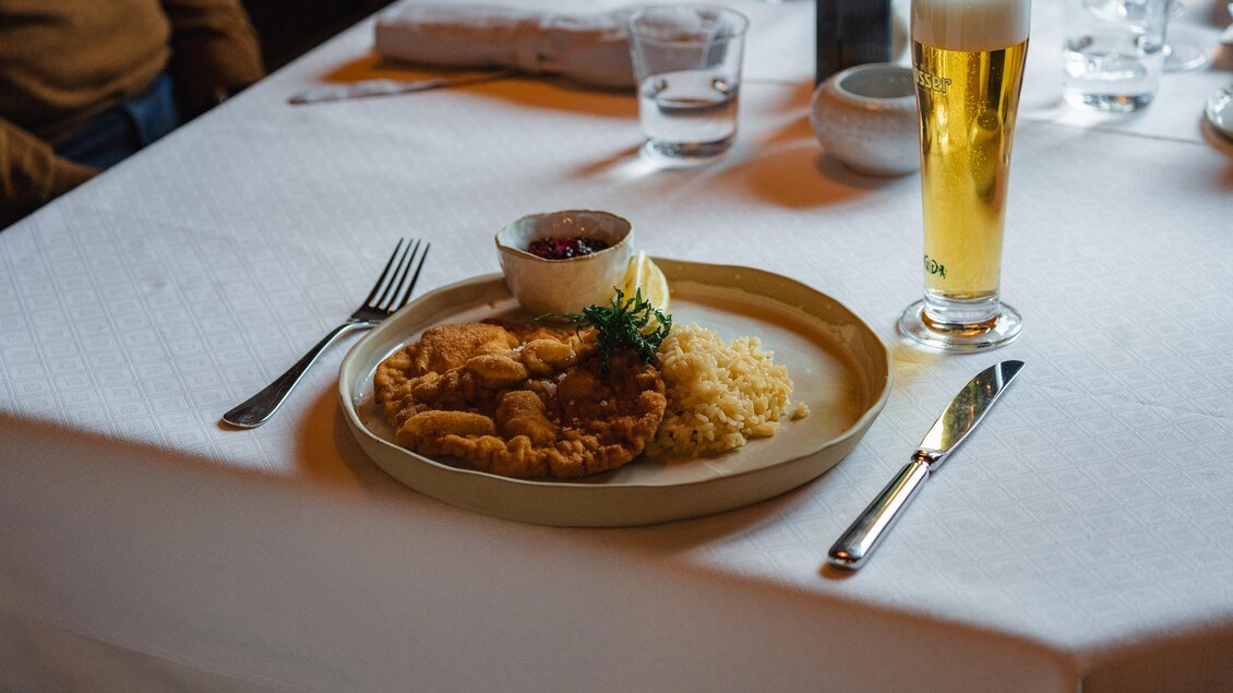 Ein Teller mit gebratenem Fisch und Reis, dazu eine Sauce und eine Zitronenscheibe. Neben dem Gericht steht ein Glas Bier auf dem Tisch.