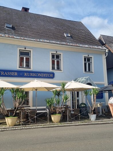 A café with a blue building and outdoor tables. Umbrellas and plants create an inviting atmosphere. | © Erlebnisregion Murtal