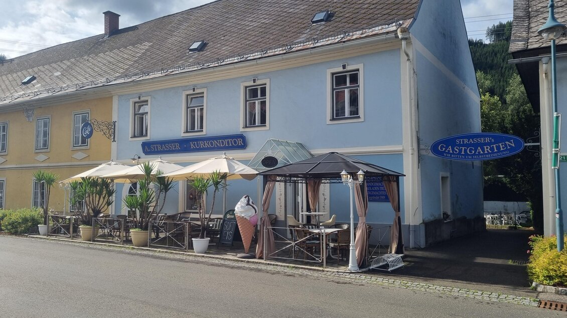 Ein Restaurant mit einem blauen Außenanstrich und einem angrenzenden Außenbereich. Es gibt einen Pavillon und Tische unter Sonnenschirmen. | © Erlebnisregion Murtal