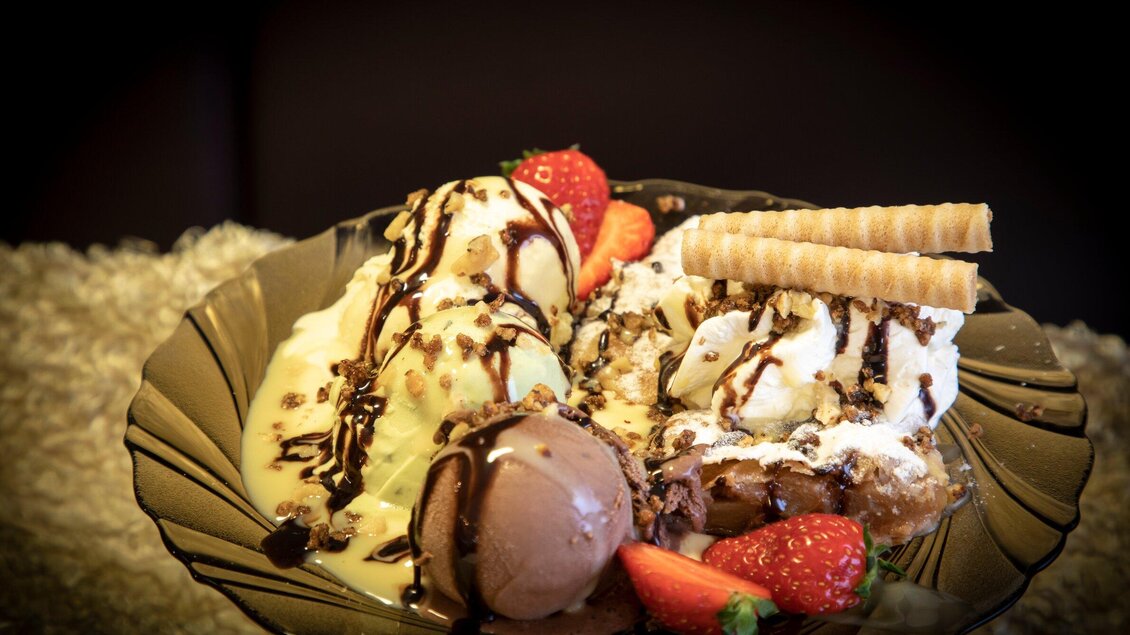 Ein köstliches Eis mit verschiedenen Sorten, Schlagsahne, Schokoladensauce und frischen Erdbeeren. Dazu sind Waffelröllchen dekorativ angeordnet. | © TV Region Graz - Lunghammer
