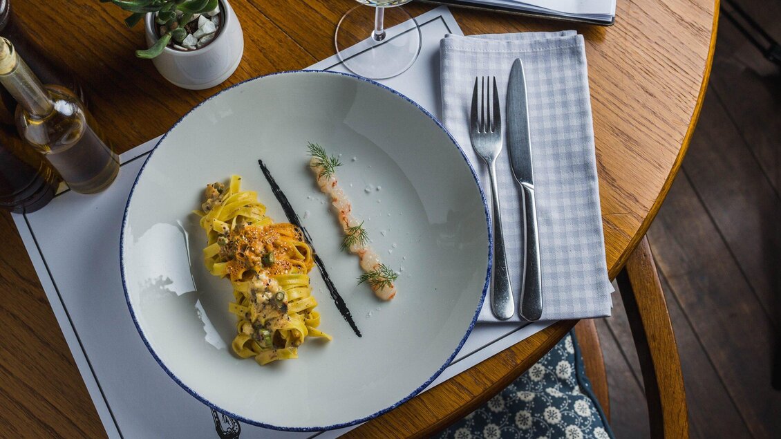 Ein schön angerichteter Teller mit Pasta, garniert mit frischen Kräutern. Darauf liegt eine elegante Soße und das Geschirr ist auf einem holzfarbenen Tisch platziert. | © Kornati