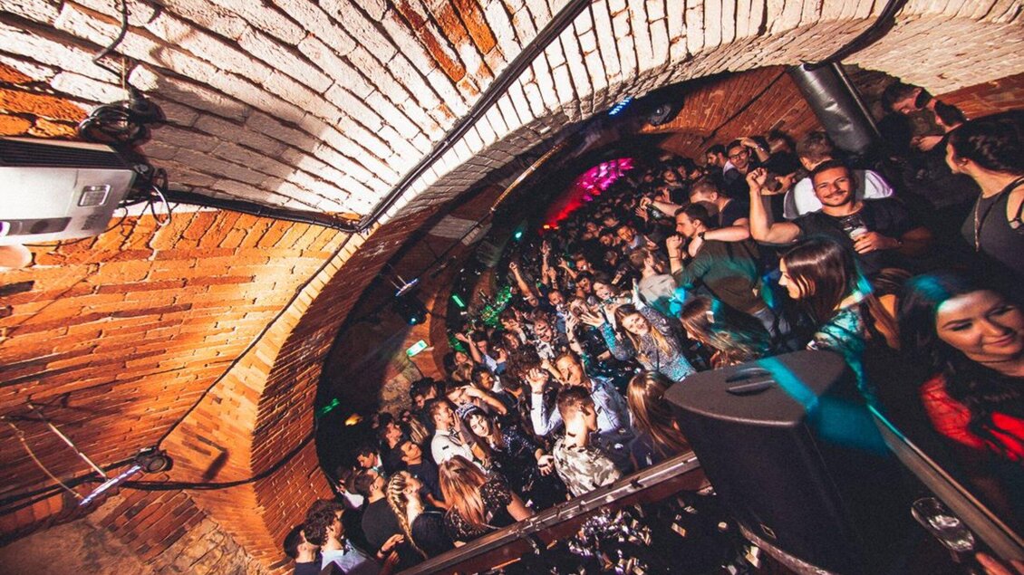 Eine lebhafte Partyszene in einem Keller mit Ziegelwänden. Viele Menschen tanzen und genießen die Musik in einer festlichen Atmosphäre. | © Kottulinsky