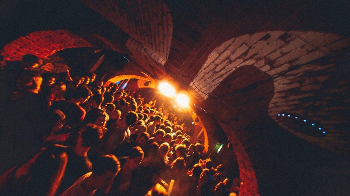 Eine lebendige Partyszene in einem Gewölberaum mit vielen Menschen. Die Atmosphäre ist energiegeladen, erleuchtet von orangefarbenem Licht. | © Kottulinsky