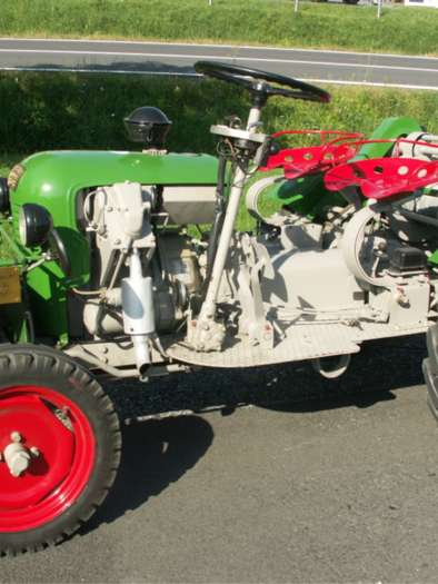 Ein klassischer Traktor mit grünem Lack und roten Rädern. Er steht auf einer Straße vor einer grünen Wiese. | © Krassermuseum