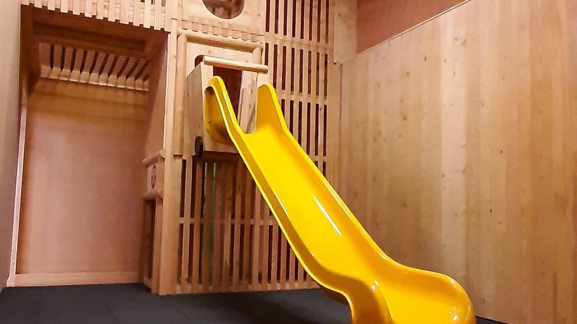Eine gelbe Rutsche in einem Holzspielraum. Der Raum ist hell und mit Holzvertäfelung gestaltet. | © JUFA Hotels