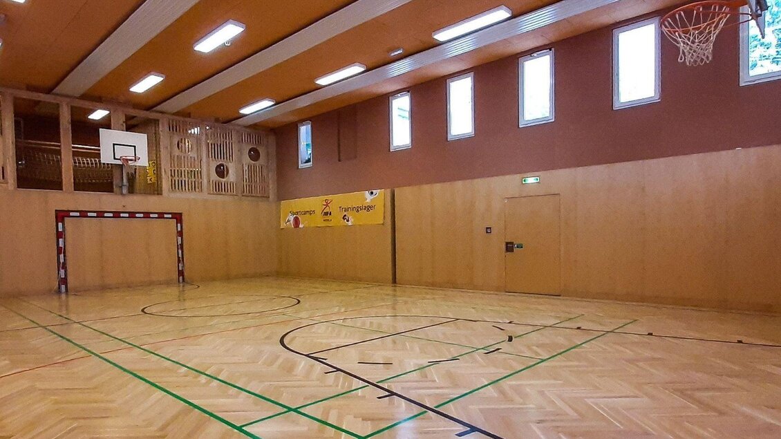 Eine Sporthalle mit einem Basketballkorb und einem Handballtor. Der Boden ist aus Holz und die Wände sind hellbraun gestrichen. | © JUFA Hotels