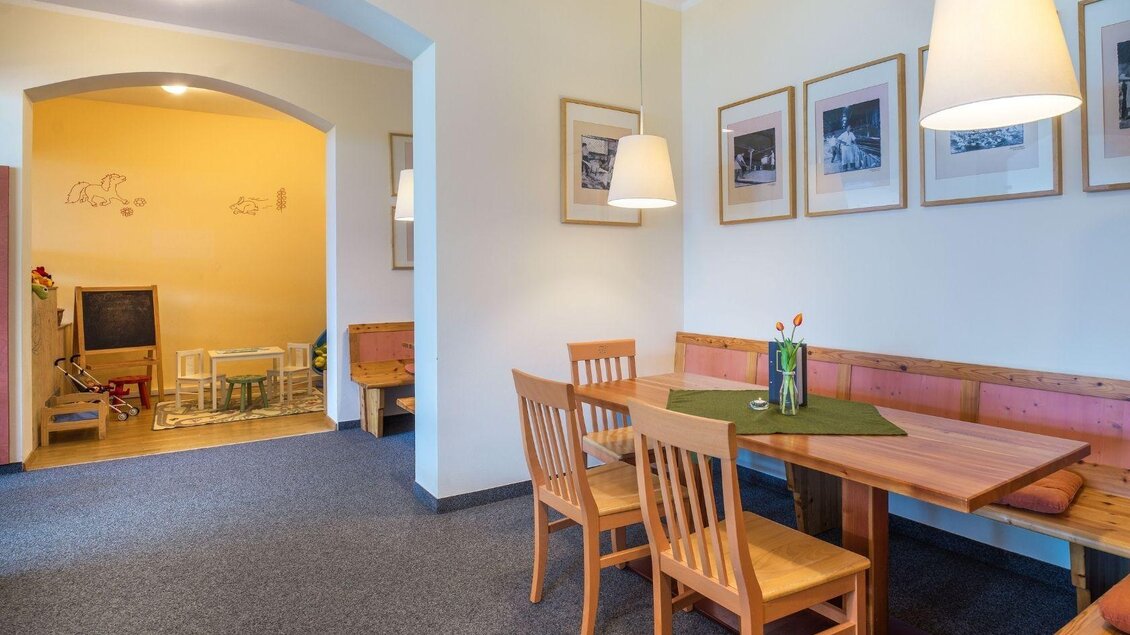 Ein einladender Essbereich mit Holzstühlen und einem Tisch. Im Hintergrund befindet sich ein Spielbereich für Kinder. | © JUFA Hotels
