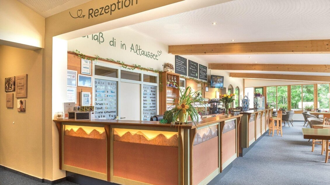 Ein einladender Empfangsbereich mit einer Theke und gemütlicher Atmosphäre. Es gibt Pflanzen und Fenster, die für viel Licht sorgen. | © JUFA Hotels