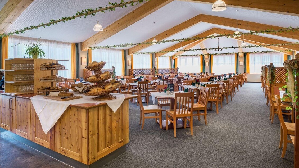 Ein gemütliches Restaurant mit Holzmobiliar und vielen Tischen. Die große Fensterfront sorgt für viel Tageslicht und eine freundliche Atmosphäre. | © JUFA Hotels