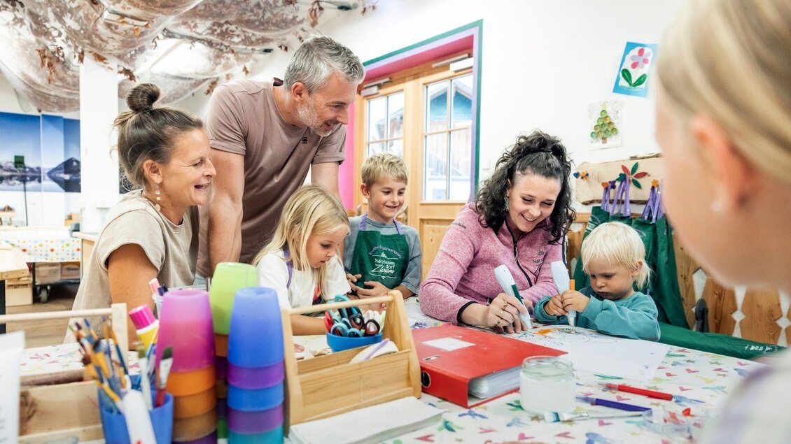 Eine Gruppe von Erwachsenen und Kindern sitzt an einem Tisch und bastelt gemeinsam. Farben, Papiere und kreative Materialien liegen verstreut auf dem Tisch. | © www.zloam.at