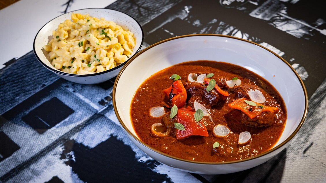 Ein köstlicher Eintopf mit Fleisch, Paprika und Zwiebeln, serviert in einer schönen Schale. Daneben befindet sich ein Teller mit leckeren Nudeln. | © Kreuzwirt am Rosenberg - Werner Krug