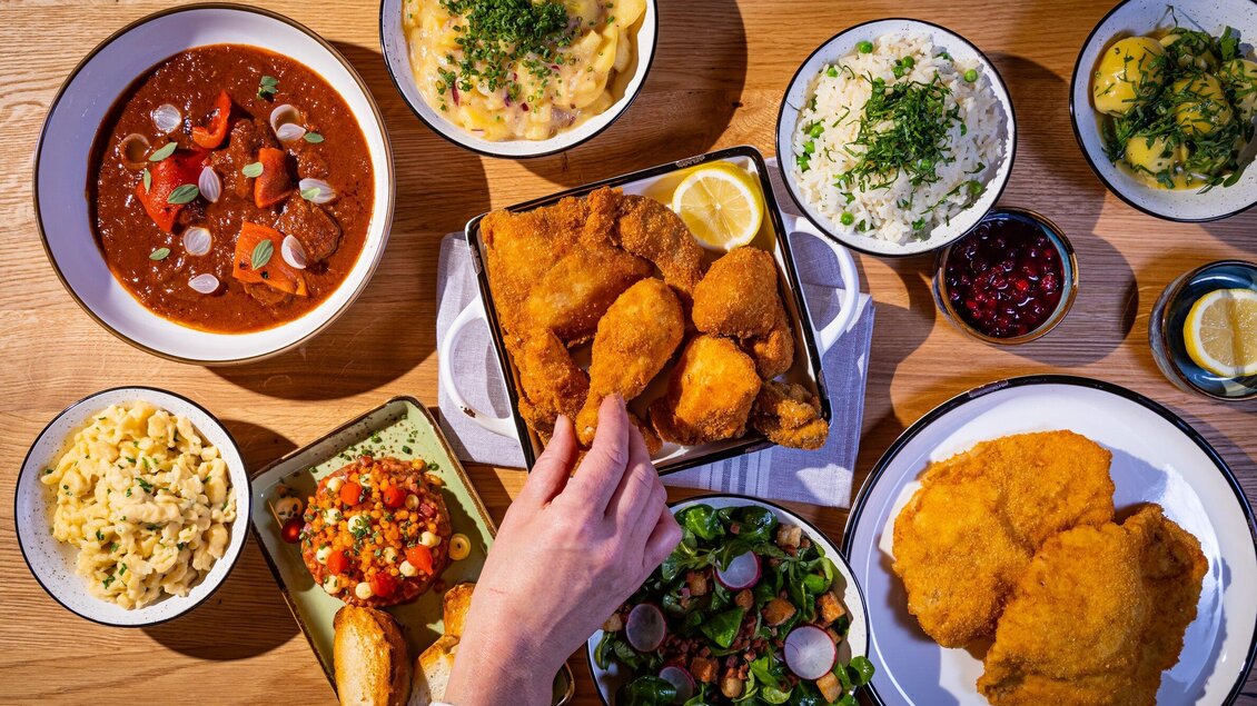 Ein Tisch voller köstlicher Gerichte, darunter gebratene Hähnchenteile, Salat, Reis und verschiedene Beilagen. Die Farben der Speisen sind frisch und einladend. | © Kreuzwirt am Rosenberg - Werner Krug