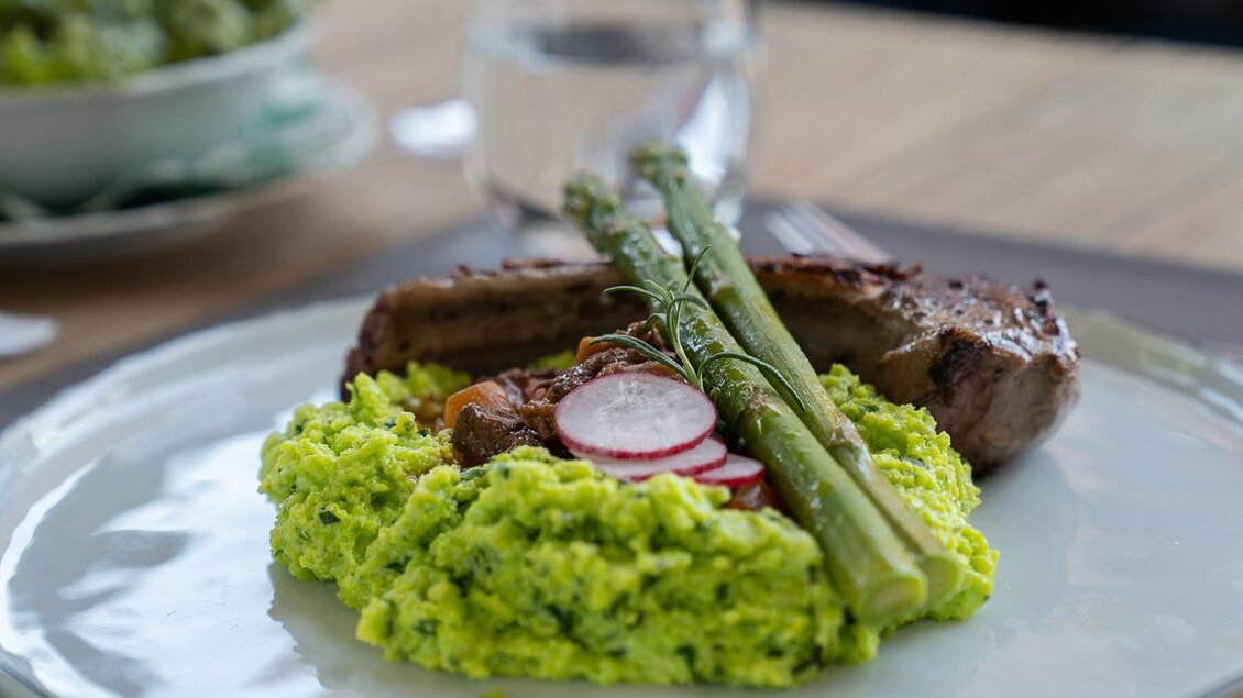Ein Teller mit grünem Püree, gegrilltem Fleisch und frischem Spargel. Dazu sind Radieschen dekoriert. | © Kreuzwirt - Matthias Schweyer