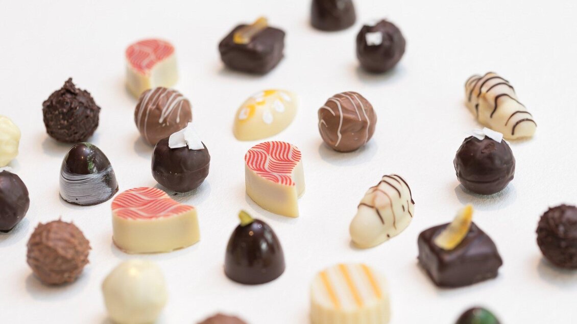Eine bunte Auswahl an Pralinen in verschiedenen Formen und Farben. Die Schokoladen reichen von dunkler bis heller Schokolade, dekoriert mit unterschiedlichen Mustern. | © Harald Tauderer und Michaela Begsteiger