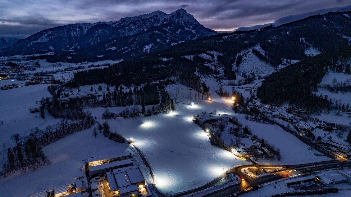 Eine schneebedeckte Landschaft bei Nacht mit beleuchtetem See. Im Hintergrund sind Berge und eine ruhige, winterliche Atmosphäre zu sehen. | © Stadtgemeinde Trofaiach