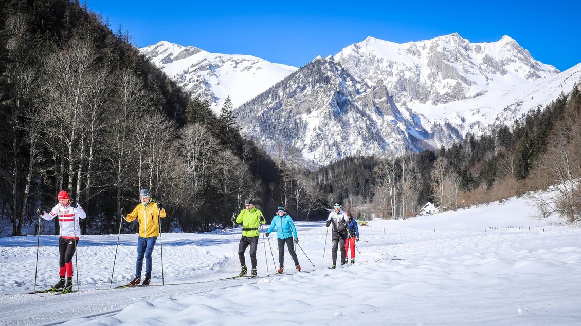 Eine Gruppe von Skifahrern bewegt sich durch eine verschneite Landschaft. Im Hintergrund sind majestätische Berge unter blauem Himmel zu sehen. | © Foto Freisinger