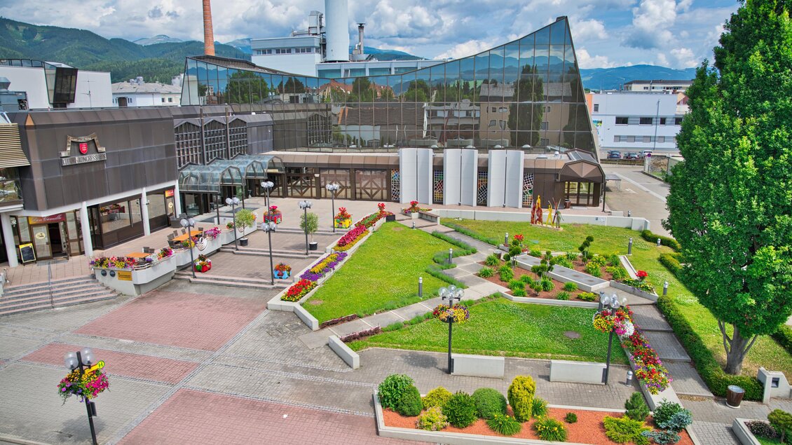Ein modernes Gebäude mit einer Glasfassade und einem gepflegten Garten. Umgeben von bunten Blumen und grünen Sträuchern bietet der Platz eine einladende Atmosphäre. | © Kulturhaus Knittelfeld