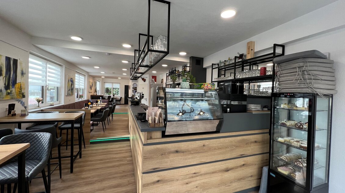 Ein modernes Café mit hellen Holzoberflächen und einer einladenden Theke. Es gibt Sitzplätze mit Stühlen und Tischen sowie eine Vitrine mit verschiedenen Leckereien. | © Andreas Albrecher