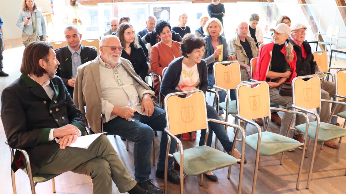 Eine Gruppe von Menschen sitzt in einem Raum und schaut in Richtung einer Bühne. Die Atmosphäre ist entspannt und die Anwesenden scheinen an einer Veranstaltung teilzunehmen. | © itshe+io