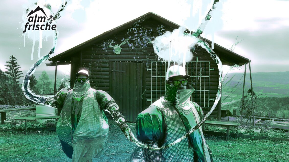 Zwei Personen in Schutzanzügen stehen vor einer Stube in der Natur. Sie scheinen Wasser oder Flüssigkeit zu spritzen, umgeben von einer malerischen Landschaft. | © itshe+io