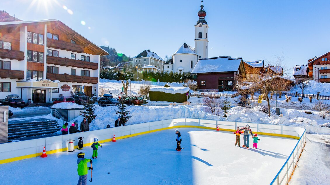 Eine eisige Schlittschuhbahn in einer verschneiten Landschaft. Im Hintergrund sind traditionelle Häuser und eine Kirche zu sehen. | © Rene Eduard Perhab