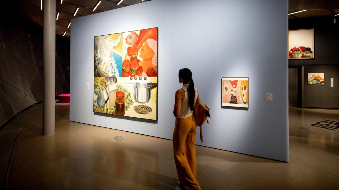 Eine Person betrachtet Kunstwerke in einer modernen Galerie. Die Wände sind hellblau gestrichen und die Bilder zeigen lebendige Farben und interessante Motive. | © Graz Tourismus - Tom Lamm