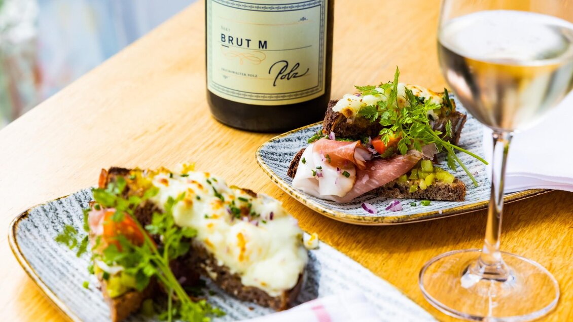 Zwei belegte Brote mit frischen Zutaten und Brut M Sekt vom Weingut Polz auf Holztisch. | © Graz Tourismus - Werner Krug