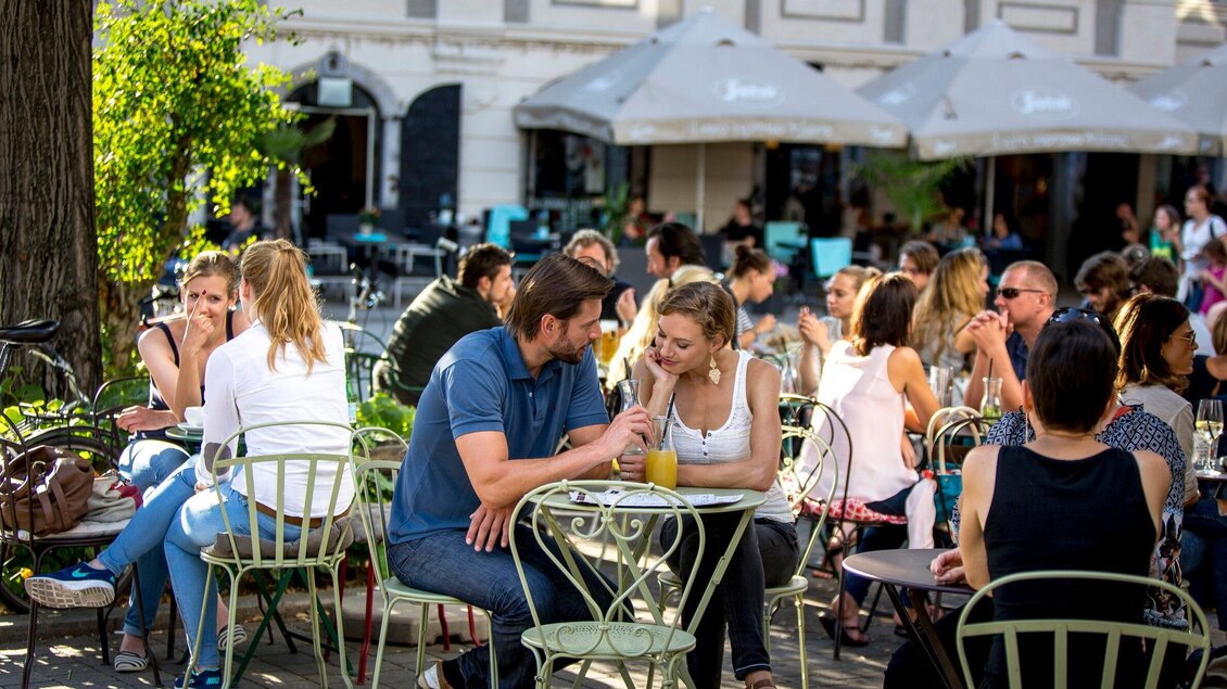 Ein belebtes Straßencafé mit vielen Gästen, die an Tischen sitzen. Paare und Gruppen genießen Getränke im Freien unter den Sonnenschirmen. | © Graz Tourismus - Tom Lamm