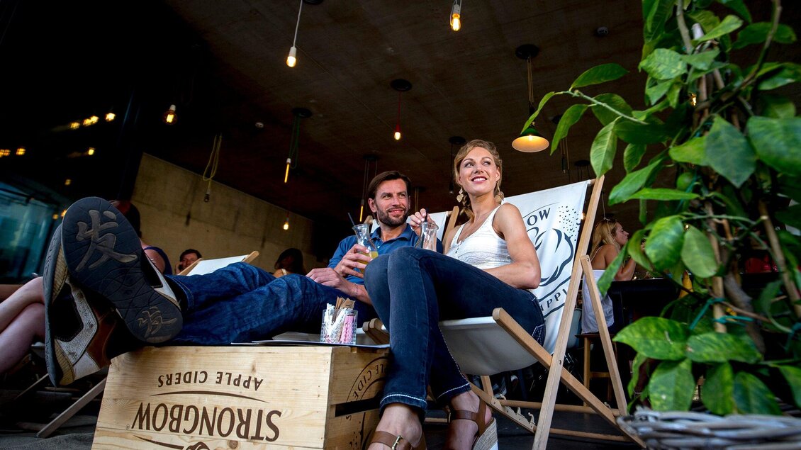 Ein Paar sitzt entspannt in einer gemütlichen Umgebung. Sie halten Getränke und genießen die Atmosphäre. | © Graz Tourismus - Tom Lamm