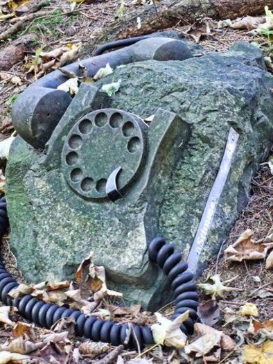 An old telephone apparatus lying on a large stone, surrounded by leaves and earth. The scene conveys a rustic and nostalgic atmosphere. | © Weges OG