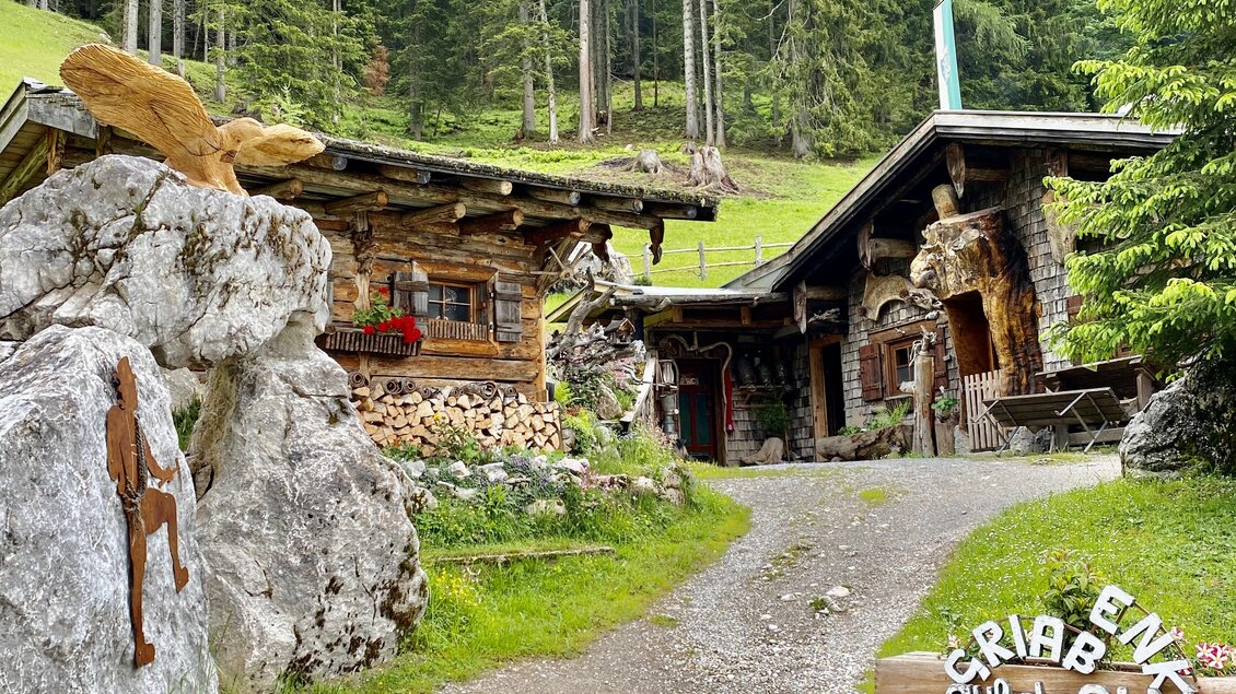 Ein gemütlicher Hüttenkomplex inmitten einer grünen Landschaft. Im Hintergrund erheben sich hohe Bäume und eine sanfte Berglandschaft. | © ©KajetanGerharter 