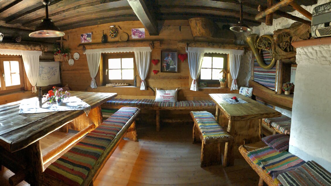 Ein rustikales, gemütliches Zimmer mit Holzmöbeln und bunten, gestreiften Bänken. Große Fenster lassen viel Licht herein und schaffen eine einladende Atmosphäre. | © ©KajetanGerharter 