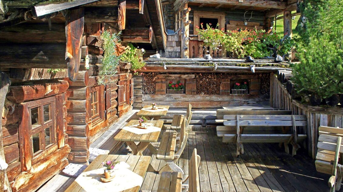 Eine rustikale Berghütte mit Holzmöbeln im Freien. Der Bereich ist von Pflanzen umgeben und strahlt eine einladende Atmosphäre aus. | © ©KajetanGerharter 