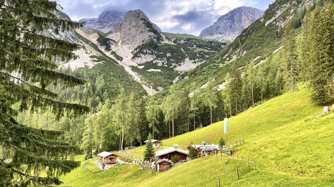 Eine malerische Landschaft mit grünen Wiesen und Bergen im Hintergrund. Kleine Almhütten sind zwischen den Bäumen versteckt. | © ©KajetanGerharter 