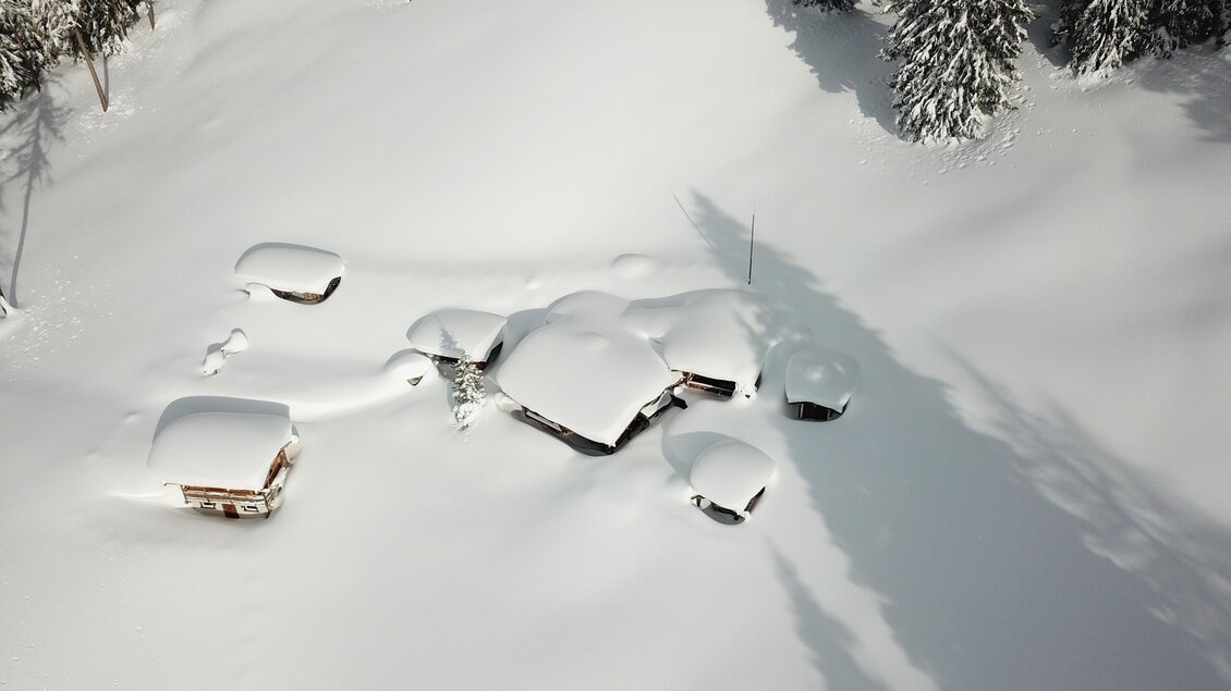 Eine ruhige Winterlandschaft mit schneebedeckten Hütten. Die Umgebung besteht aus frischem, unberührtem Schnee und hohen Tannenbäumen. | © ©KajetanGerharter 