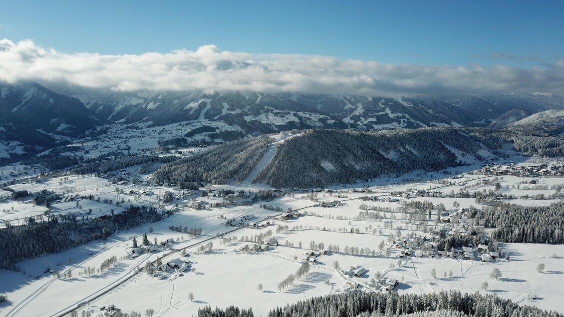 Eine malerische Winterlandschaft mit schneebedeckten Hügeln und Bäumen. Der Himmel ist klar und blau, und die Wolken liegen sanft über den Bergen. | © ©KajetanGerharter 