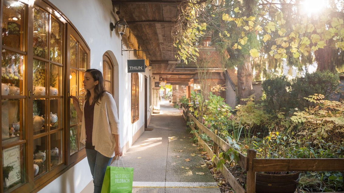 Eine Frau schaut interessiert in ein Schaufenster. Die Straße ist von Bäumen gesäumt und hat eine gemütliche Atmosphäre. | © Tourismusverband Feldbach/ B. Bergmann