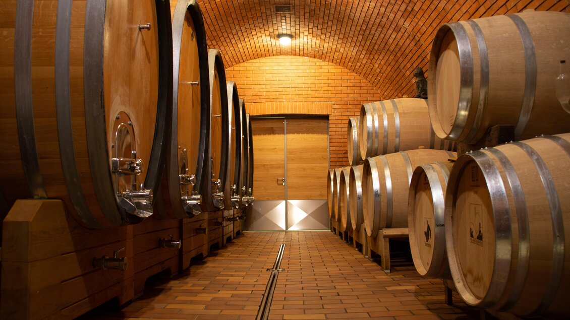 Ein Weinkeller mit großen, runden Eichenfässern an den Wänden. Die Stille und die warmen Holz- und Ziegeltonfarben schaffen eine einladende Atmosphäre. | © @Silberberg