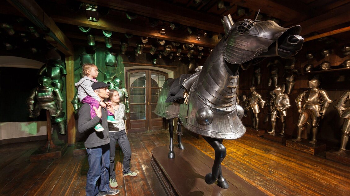 Eine Familie betrachtet eine große, gepanzerte Pferdestatue in einem Museum. Im Hintergrund sind weitere Rüstungen sichtbar. | © Graz Tourismus - Harry Schiffer